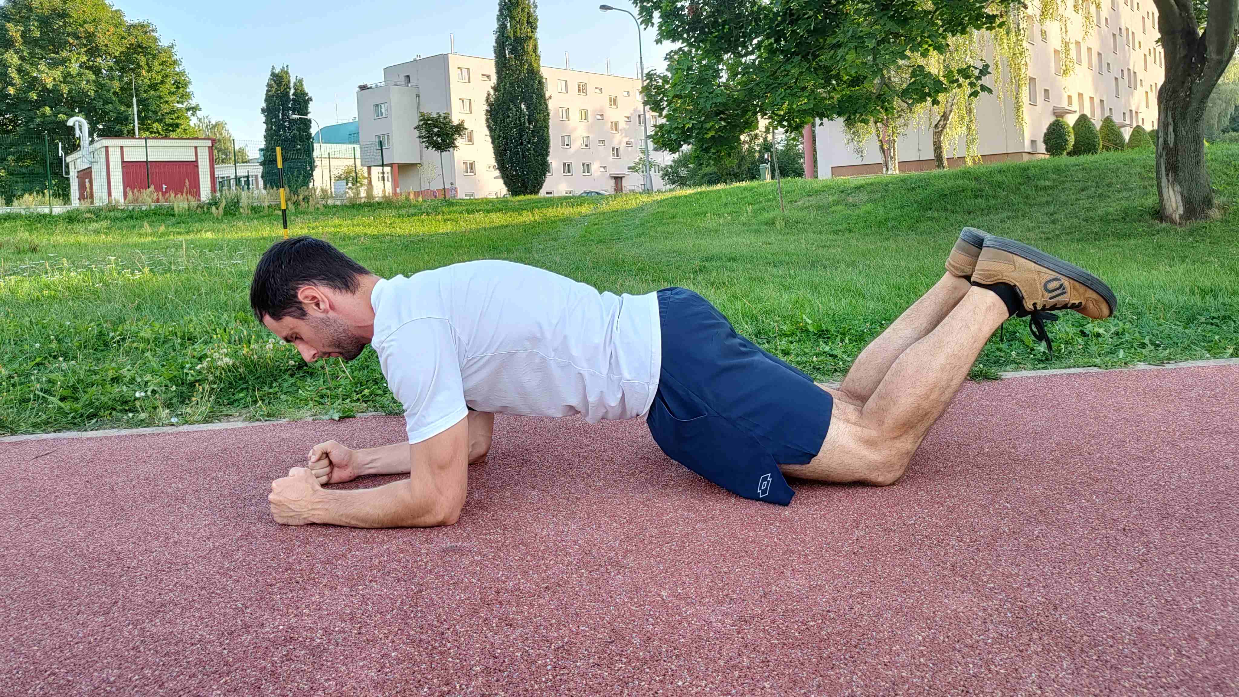 Muž cvičí klasický plank na kolenou v parku.
